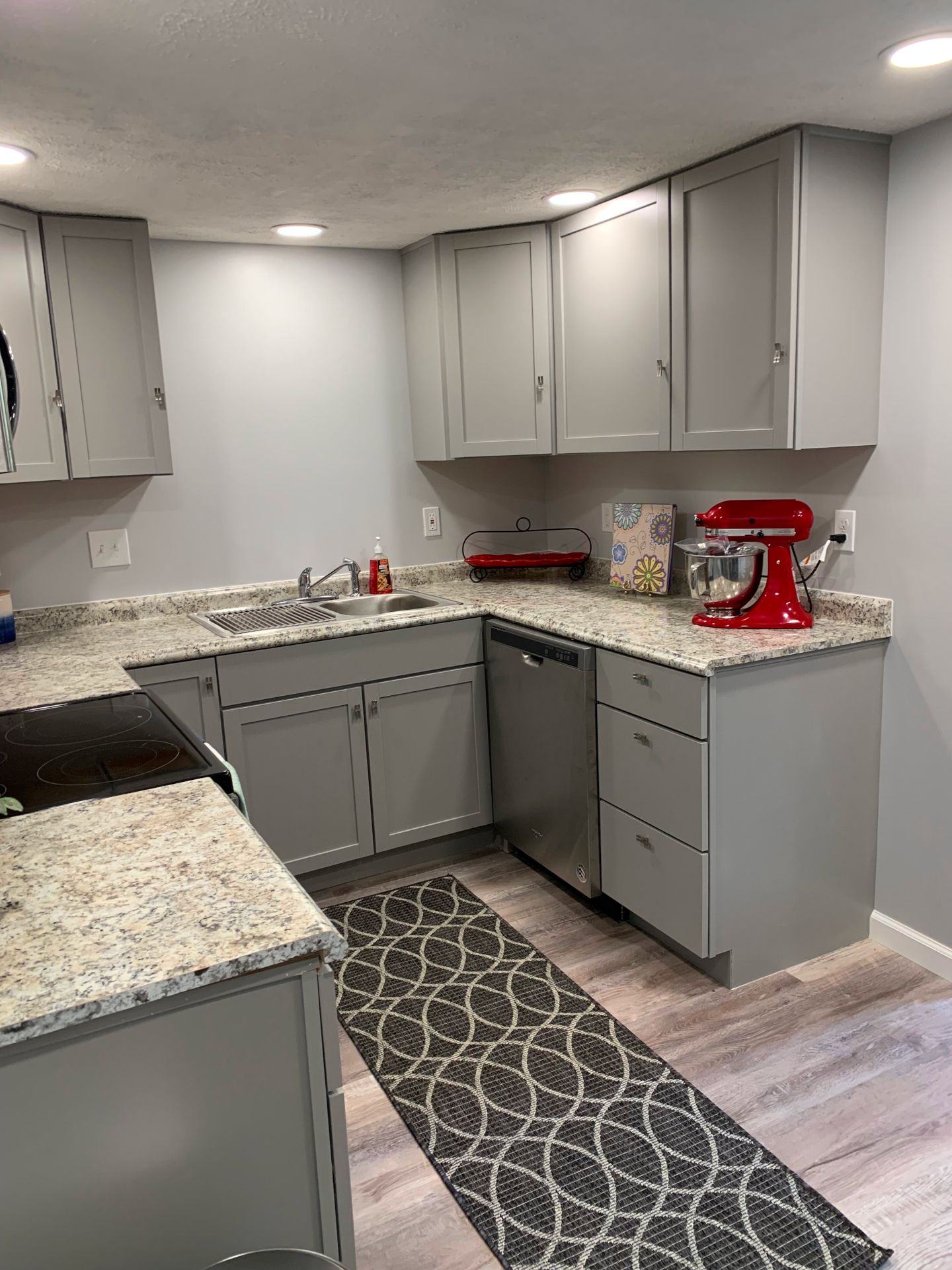 A kitchen with gray cabinets , granite counter tops , and a red mixer.