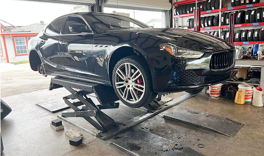 Black Maserati on a car lift in a garage, tires on shelves in background.