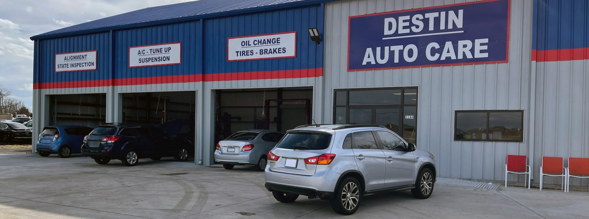 Destin Auto Care shop with cars parked outside. Blue and grey building with large sign.