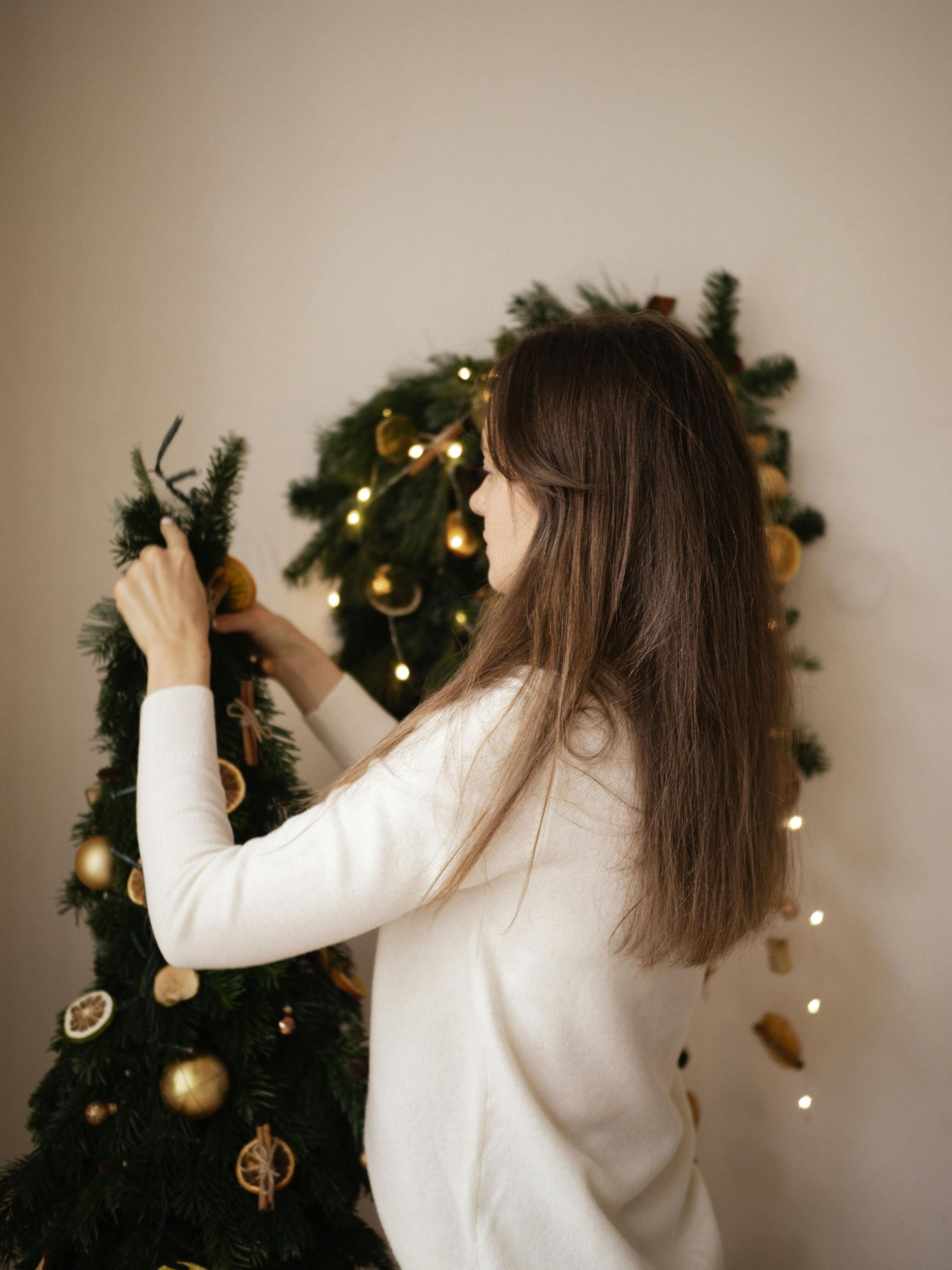A woman in a white sweater is decorating a christmas tree.