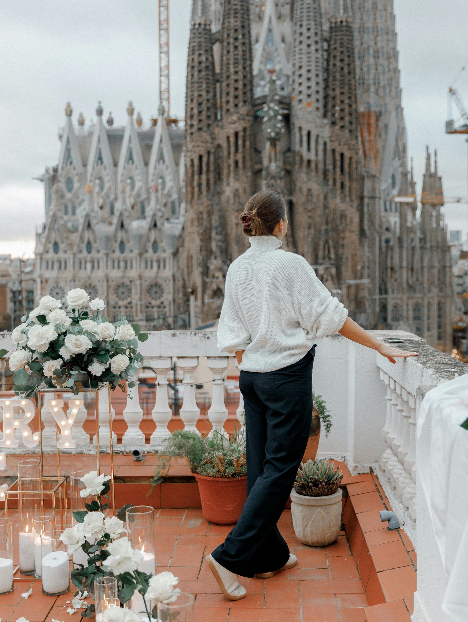 A woman in a white sweater is standing on a balcony overlooking a large building