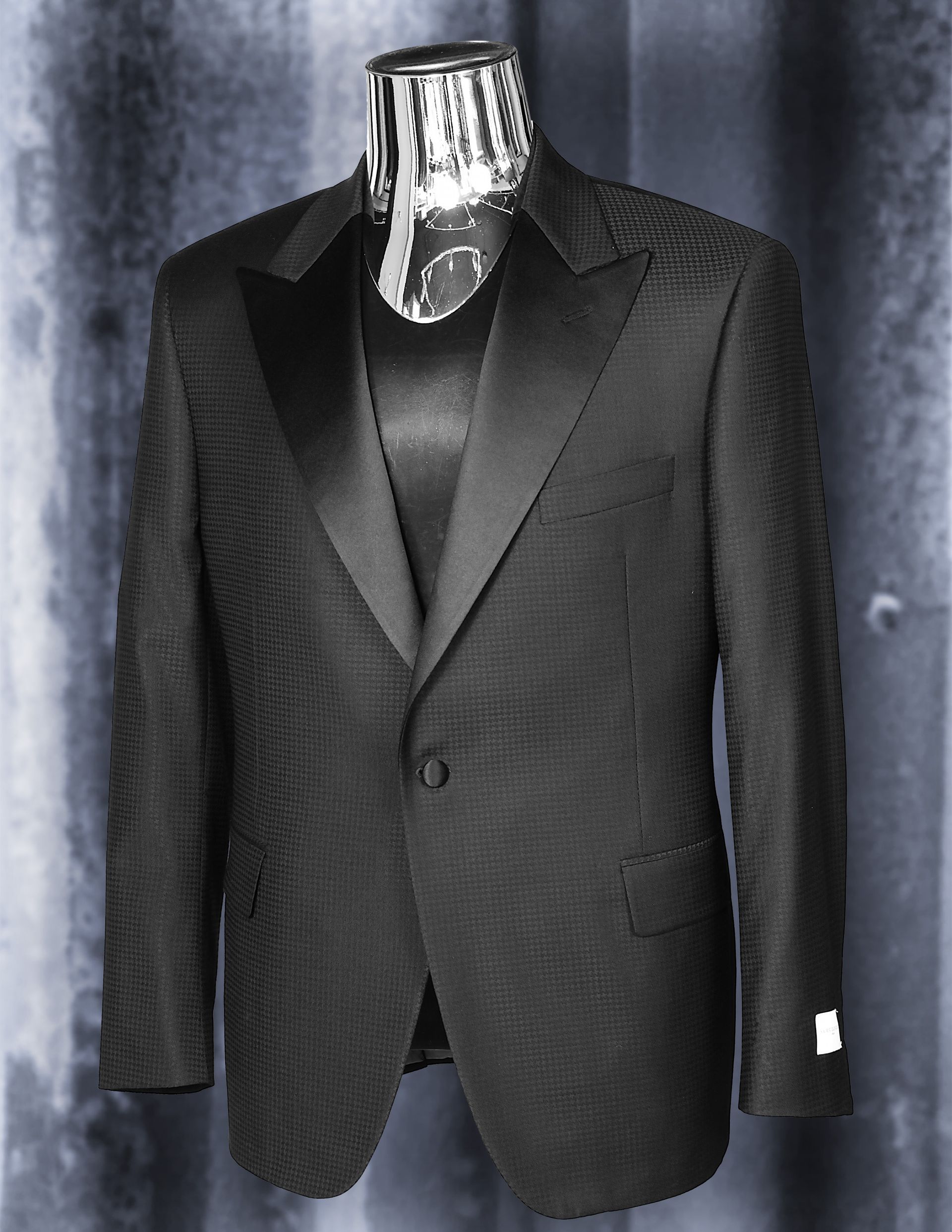 Black tuxedo jacket on a mannequin, satin lapels, against a textured gray background.