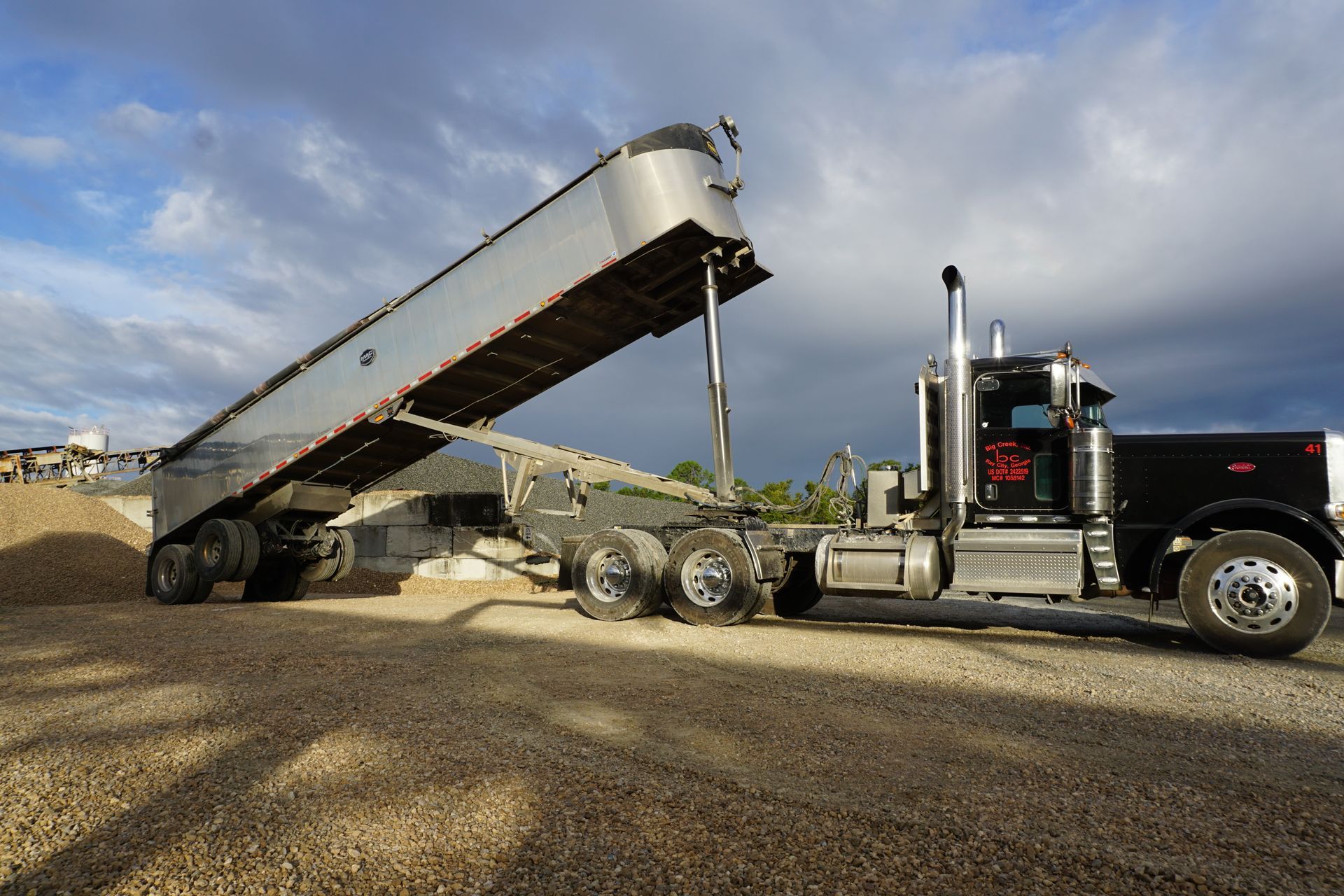A dump truck is loading a trailer with gravel.