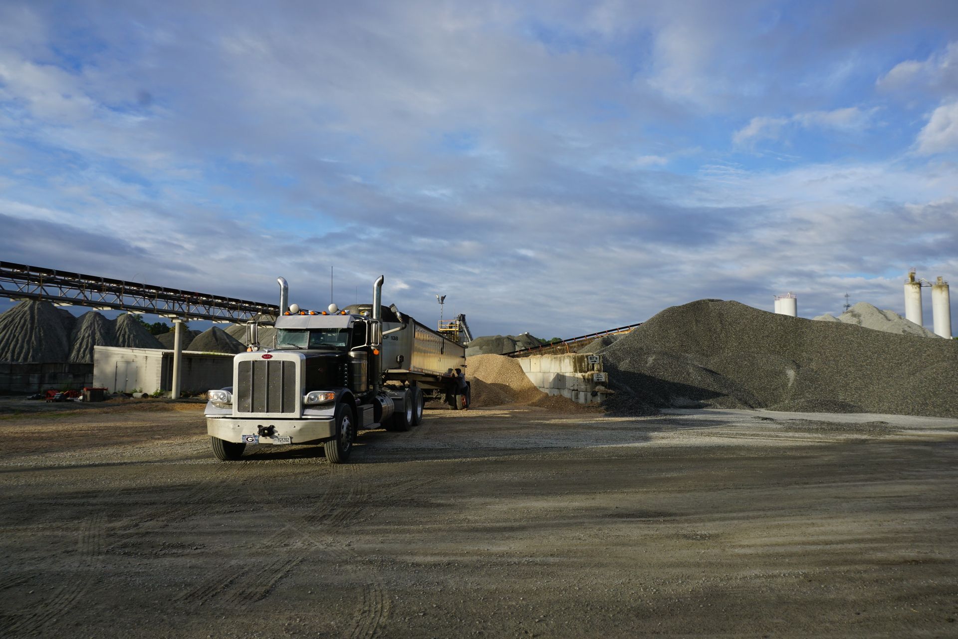 A dump truck is parked in a gravel lot in front of a pile of gravel.