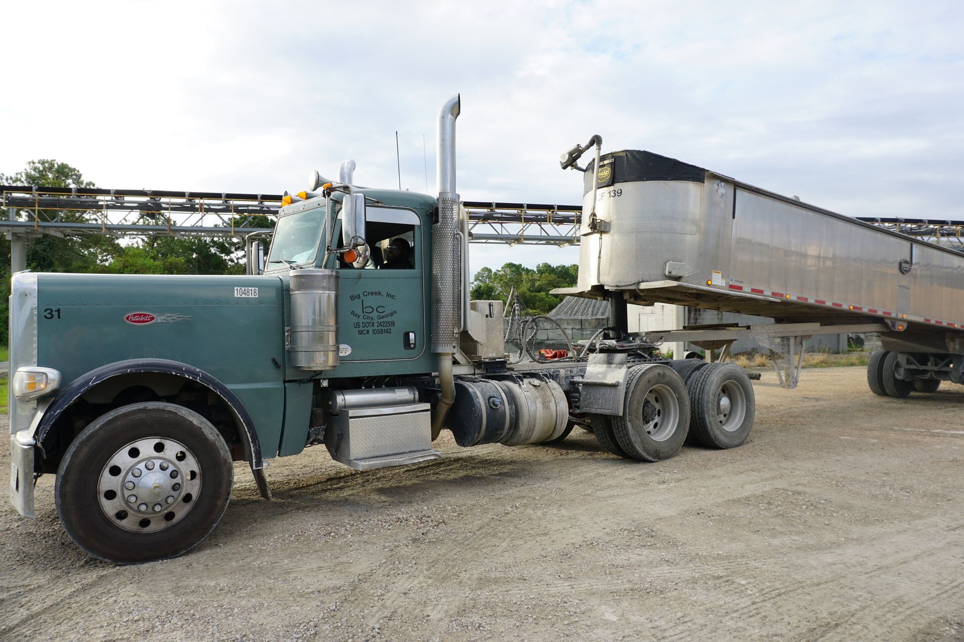 A semi truck with a trailer attached to it is parked in a gravel lot.