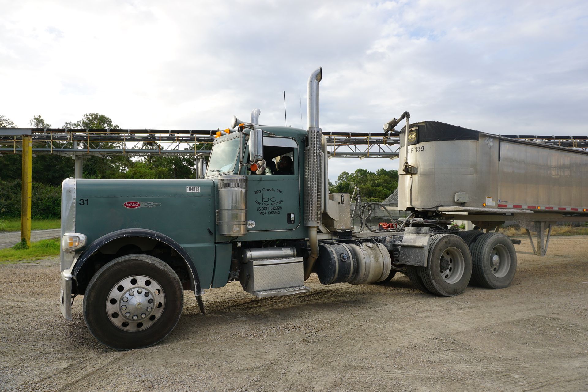 A semi truck with a trailer attached to it is parked in a gravel lot.