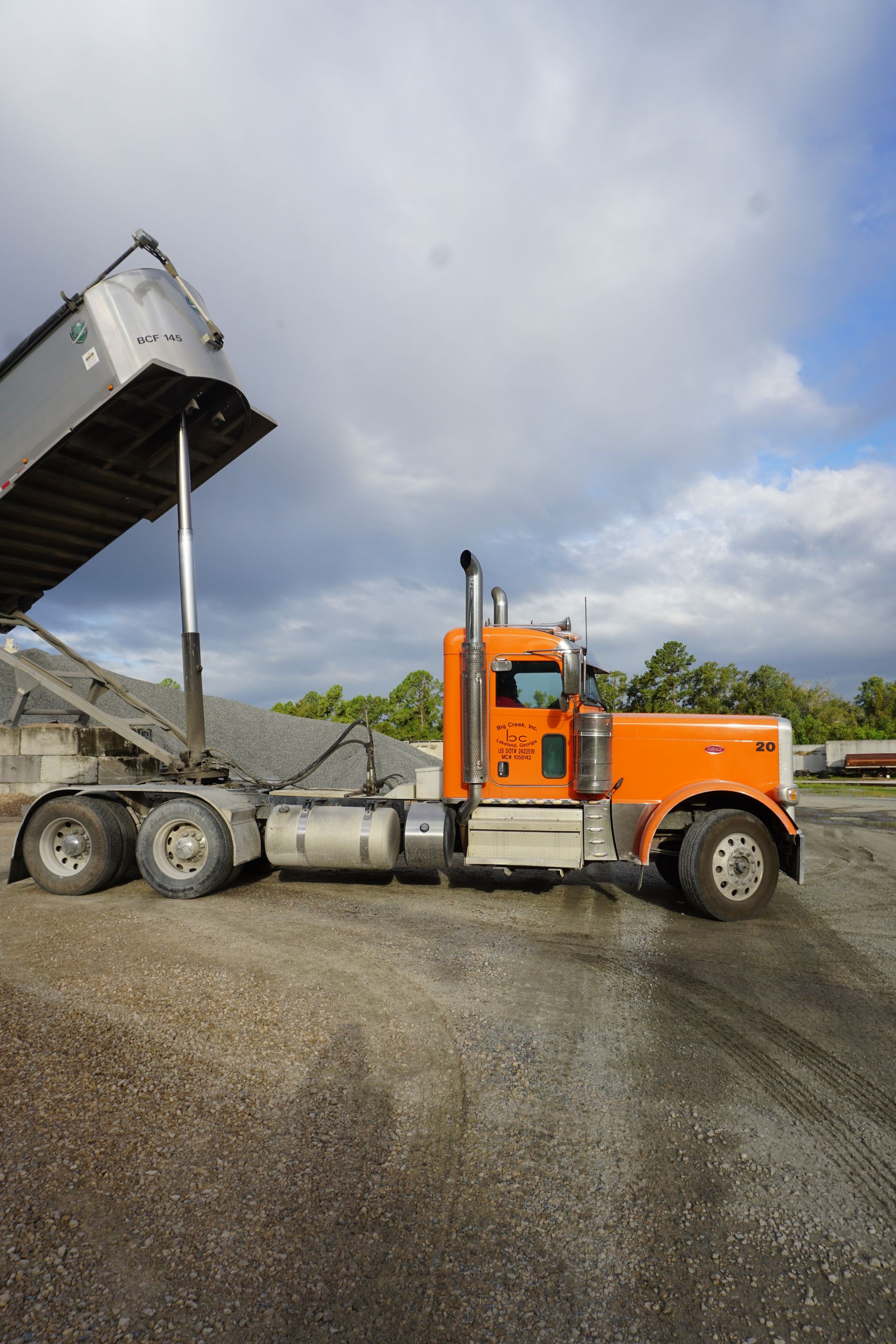 An orange dump truck is parked in a gravel lot.