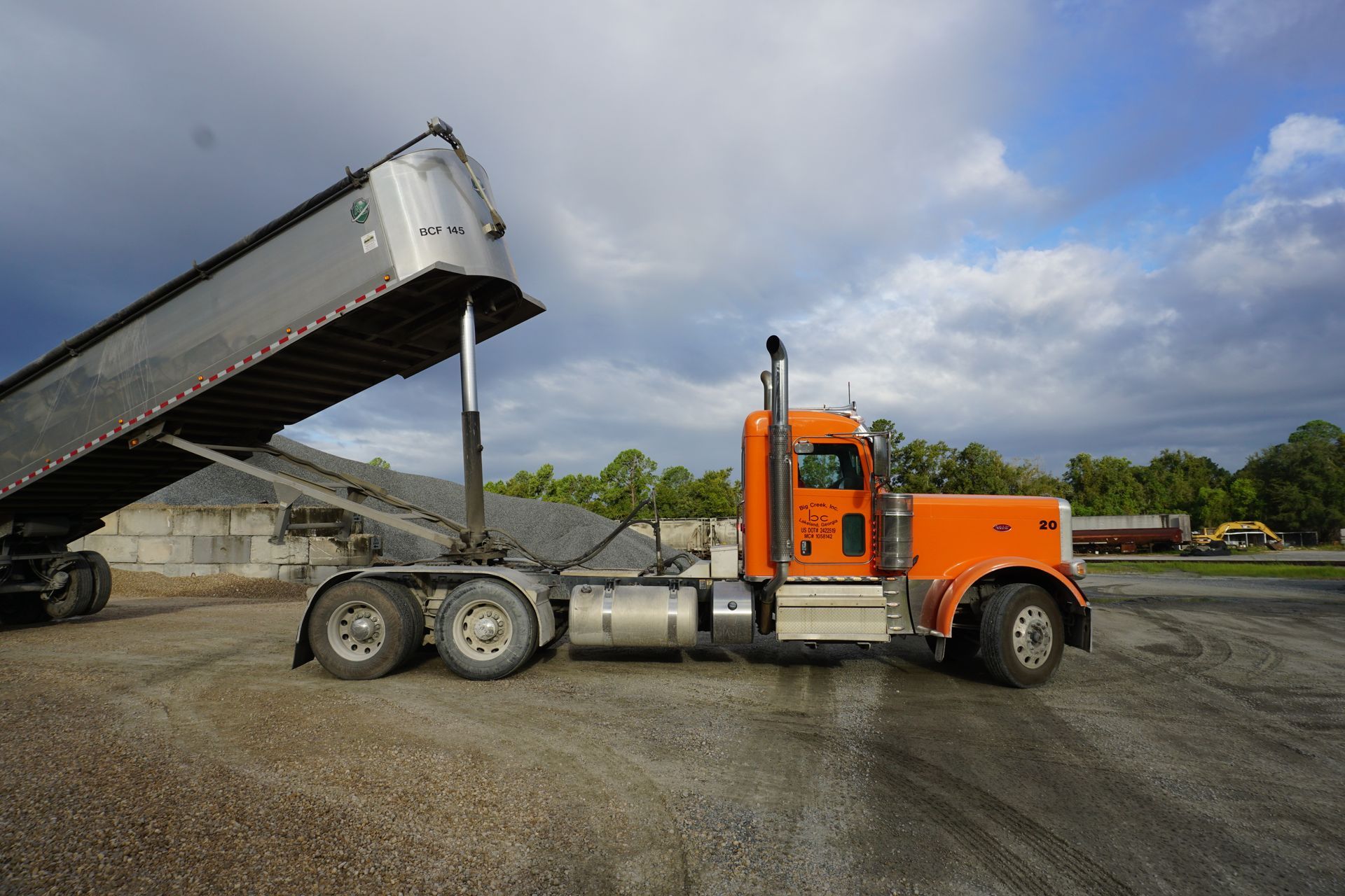 A dump truck is being loaded with gravel in a parking lot.