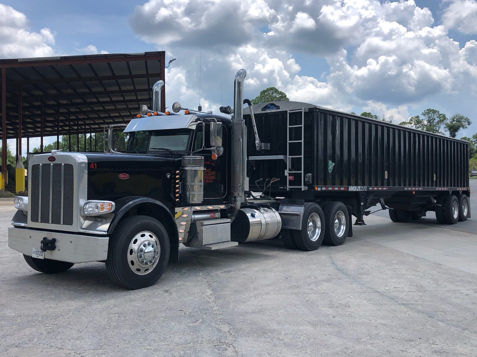 A black semi truck with a black trailer is parked in a parking lot.