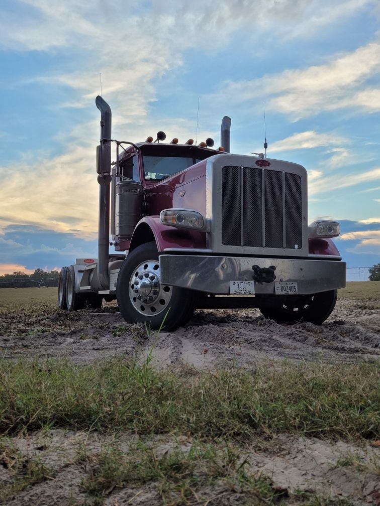 A red semi truck is parked in the middle of a dirt field.