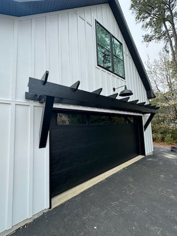A white house with a black garage door and a black pergola.