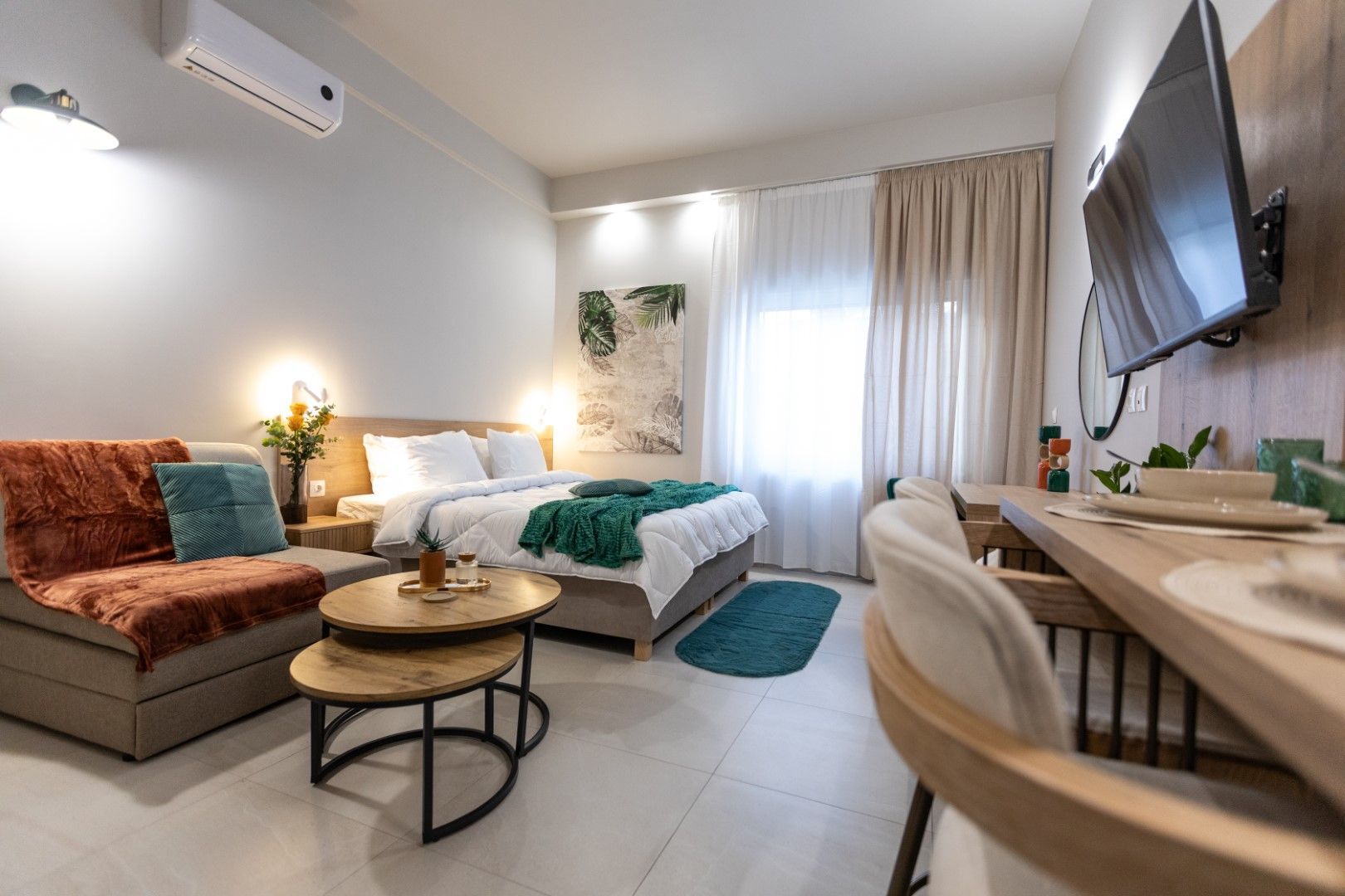 Cozy studio apartment with bed, small sofa, desk, and TV; neutral colors, well-lit.