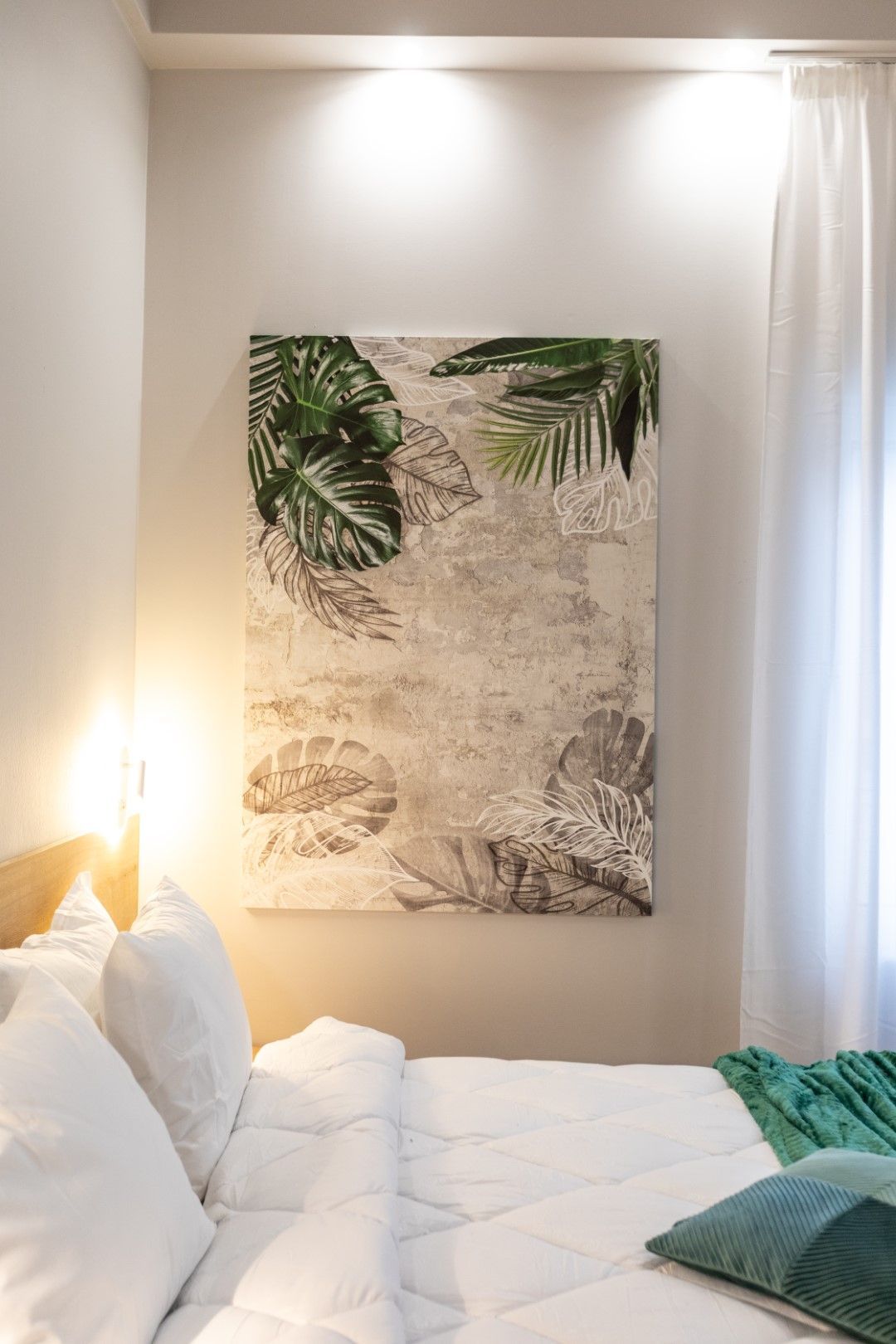 Bedroom with white bedding, art with leaves, and green accents.
