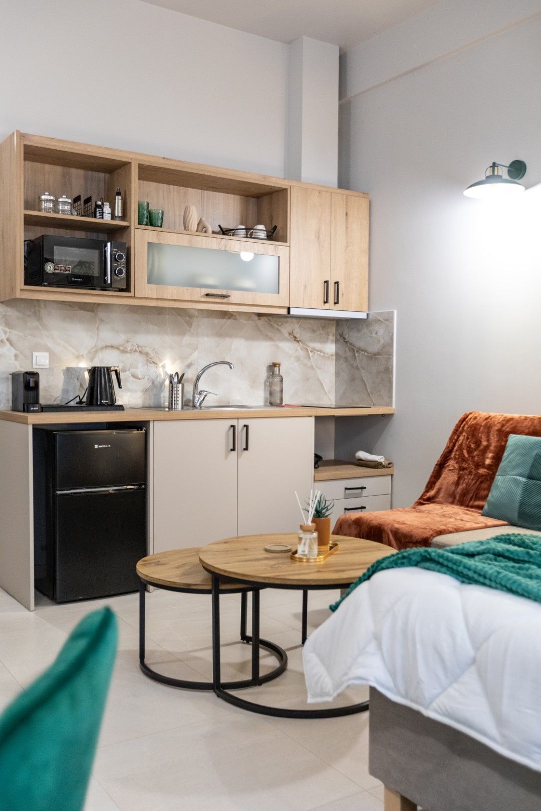 Small studio apartment with a kitchenette, small fridge, and two round coffee tables.