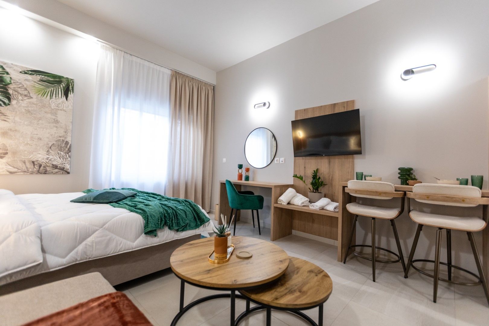 Μοντέρνο δωμάτιο ξενοδοχείου με κρεβάτι, γραφείο, τηλεόραση και καθιστικό. Ουδέτεροι τόνοι με πράσινες και ξύλινες πινελιές.