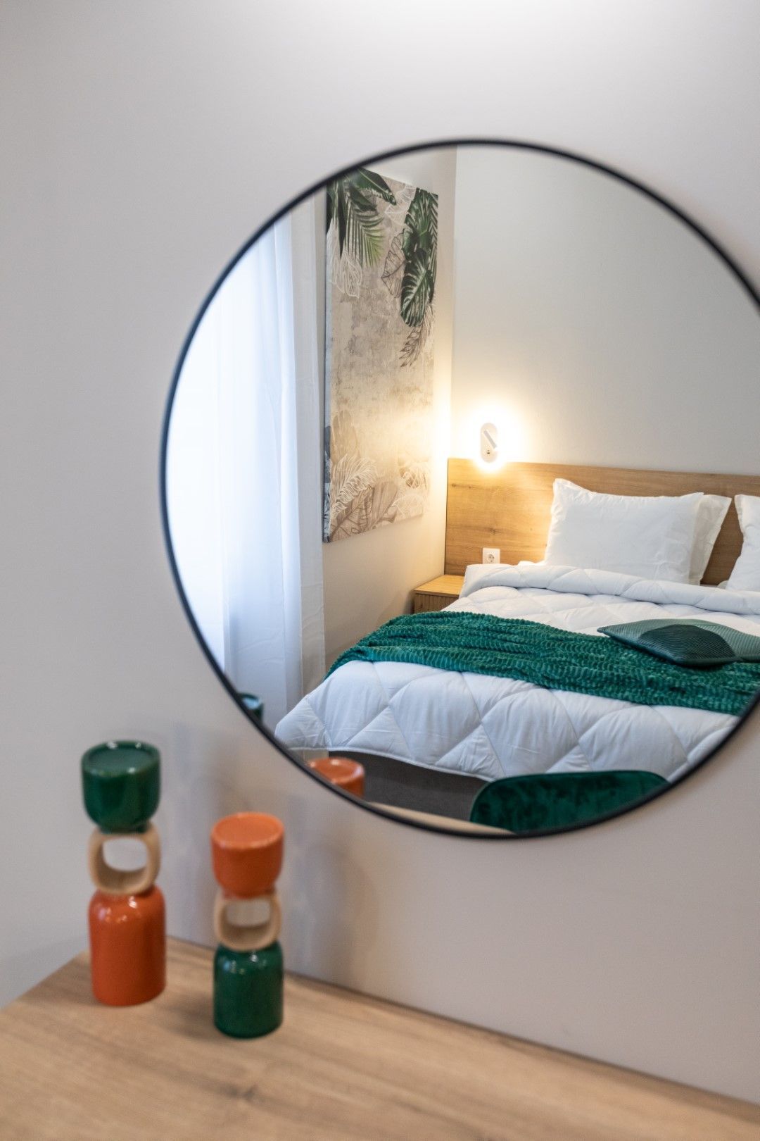 Round mirror reflecting a bedroom with a bed, green blanket, and decorative items.