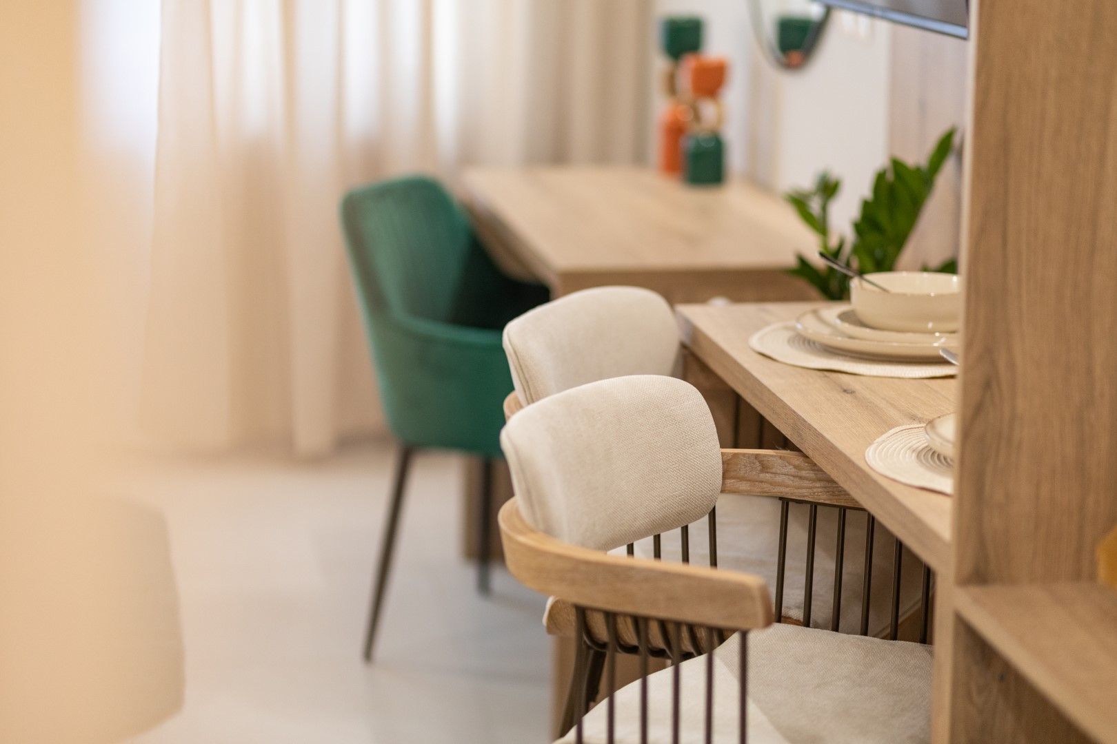 Dining area with green chair, light wood table, and two cushioned stools at a counter.