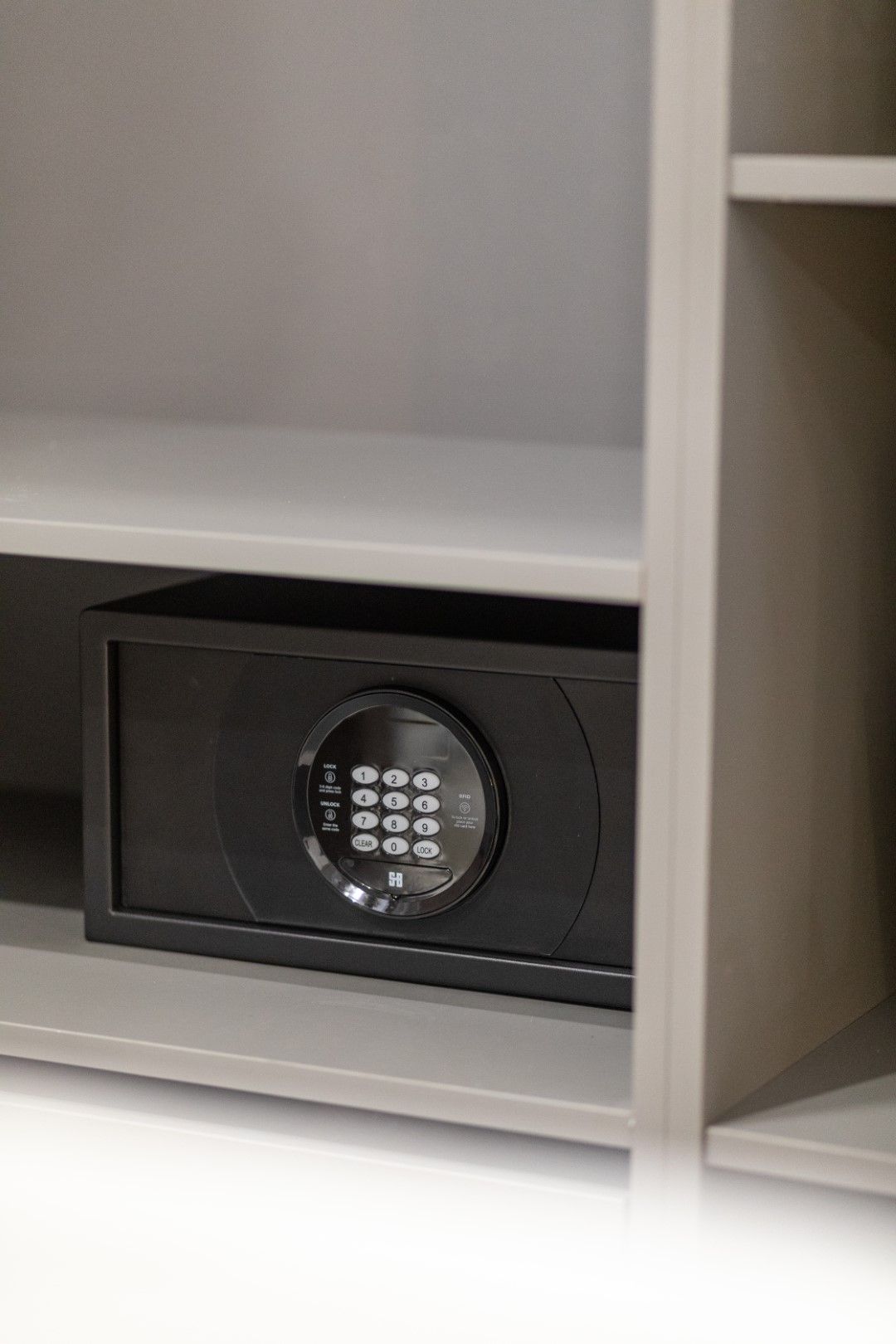 A black digital safe sits on a shelf inside a gray cabinet.