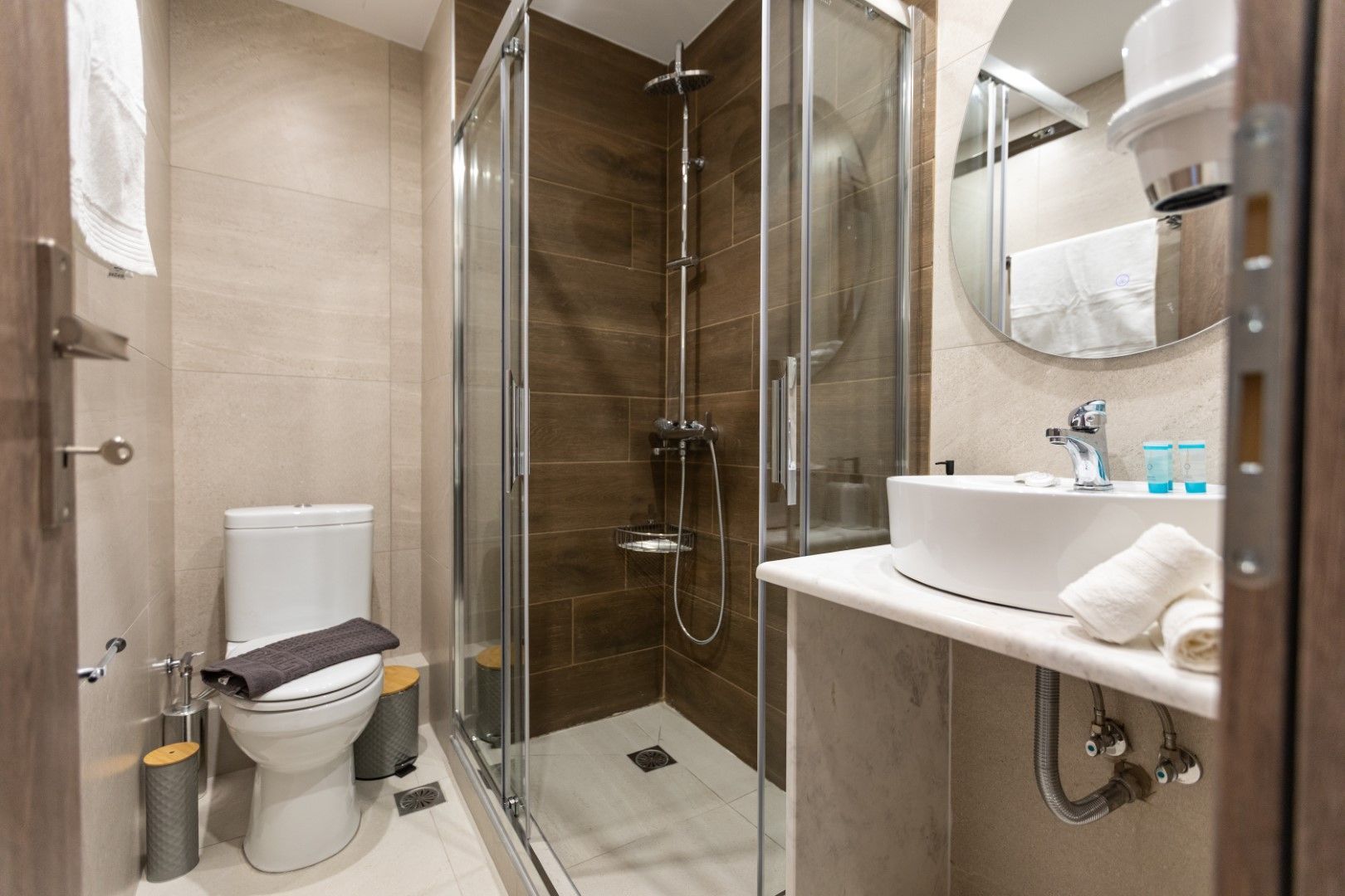 Bathroom with toilet, shower, sink, and mirror. Brown shower tile, white sink, and light walls.