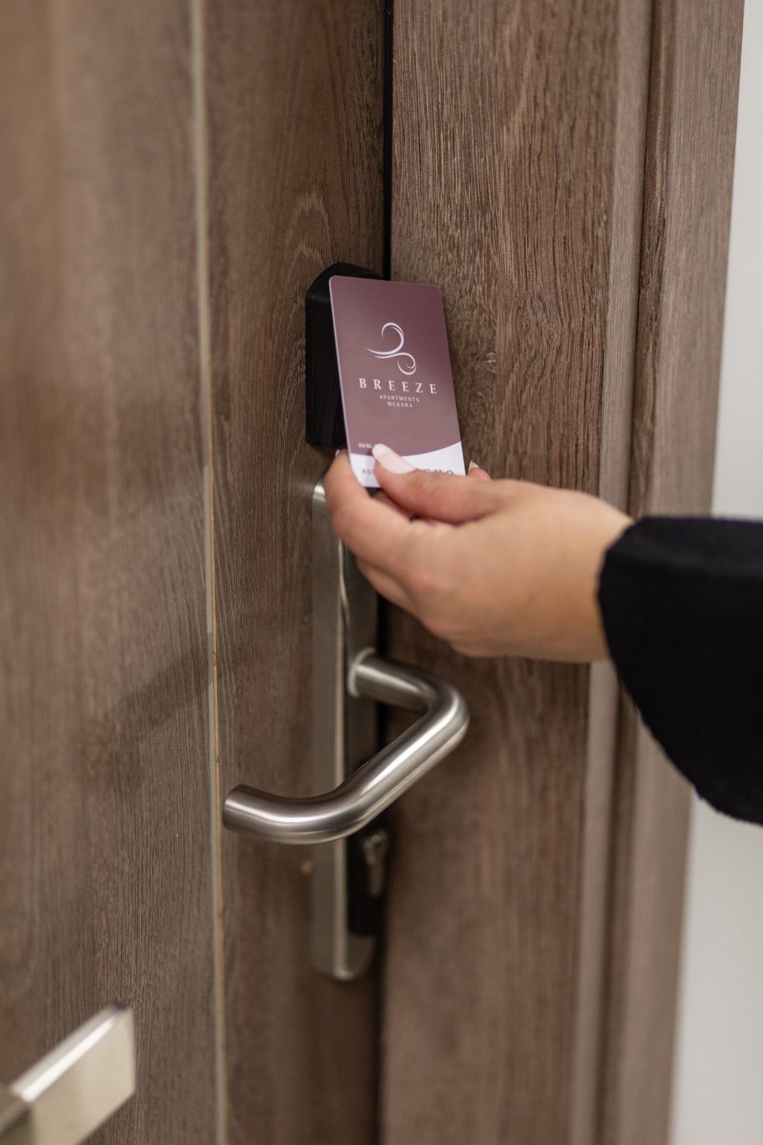Person using key card to unlock a wooden hotel room door.
