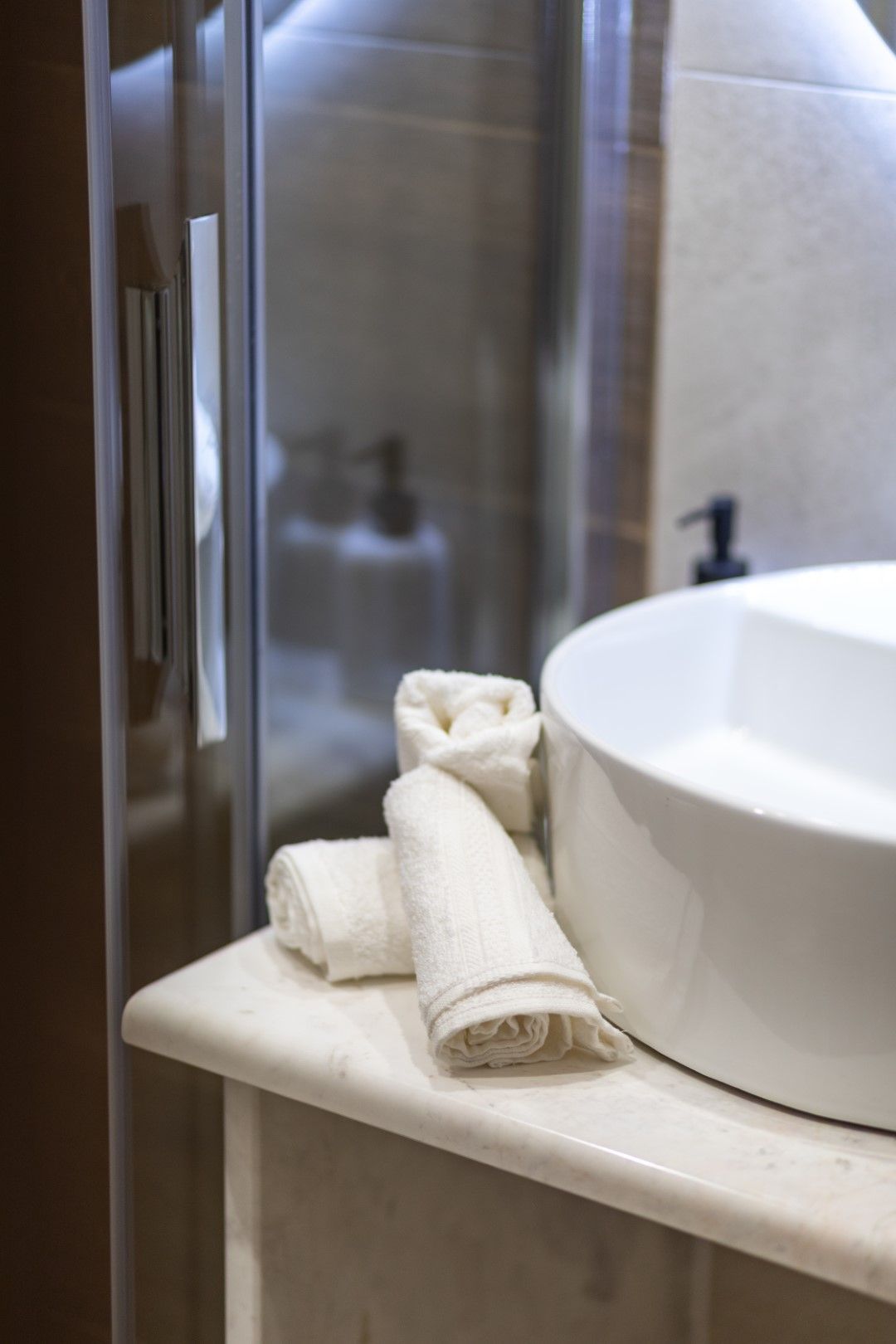 White rolled hand towels on a marble countertop next to a white sink.