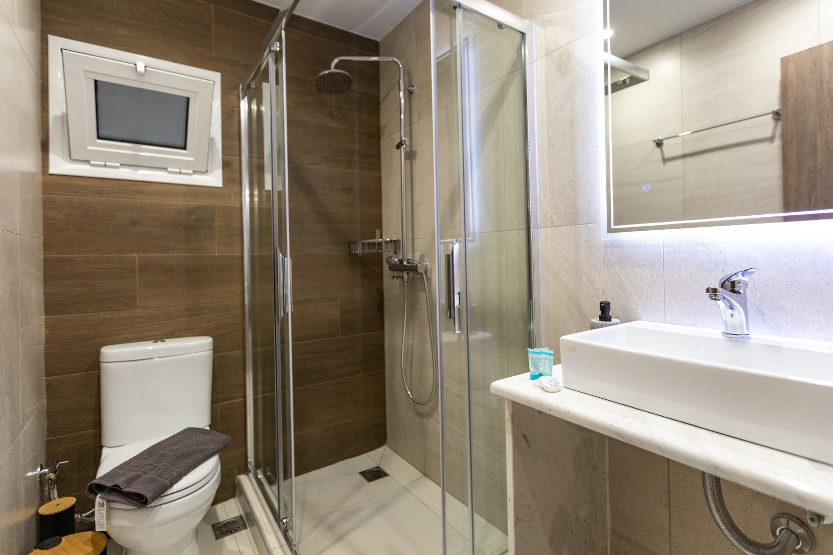 Bathroom with shower, toilet, and sink. Brown and beige tile walls. Glass shower door.