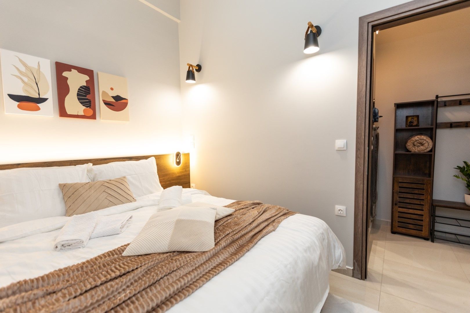 Bedroom with a large bed, brown blanket, and artwork. A doorway leads to another room.