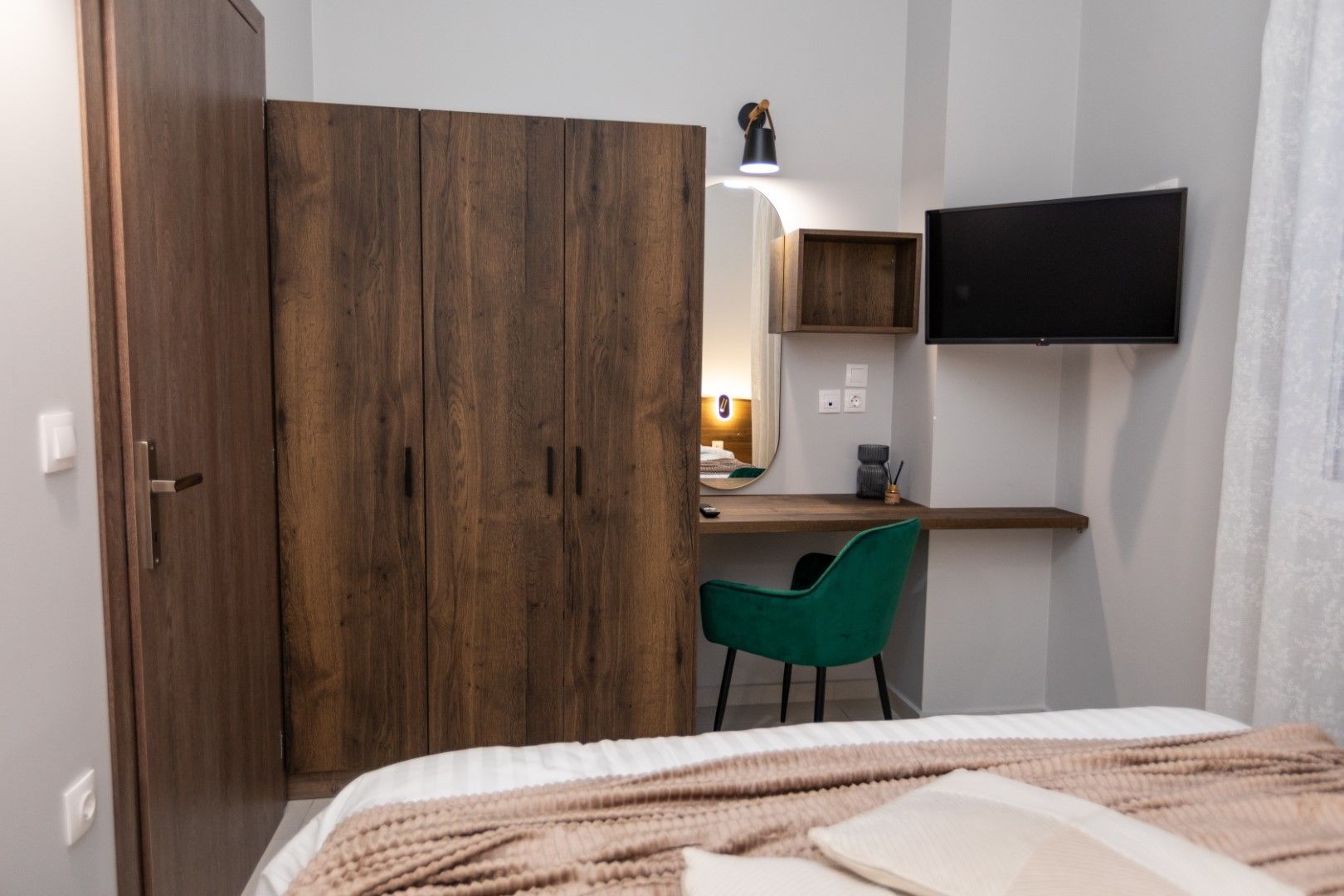 Bedroom with wooden wardrobe, desk, TV, and green chair.