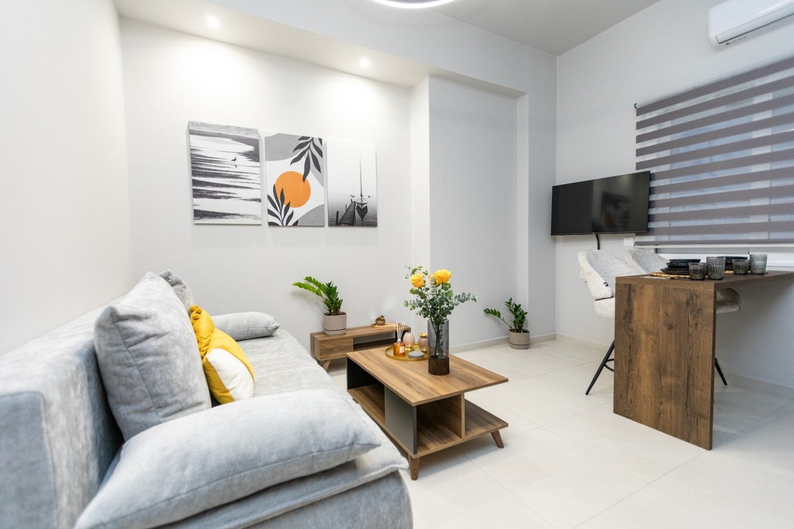 Modern living room with gray sofa, wooden coffee table, art, and desk.