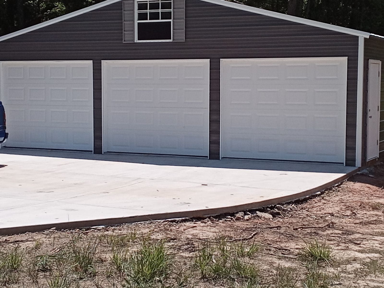 Three-bay gray garage with white doors, concrete pad, and small window.