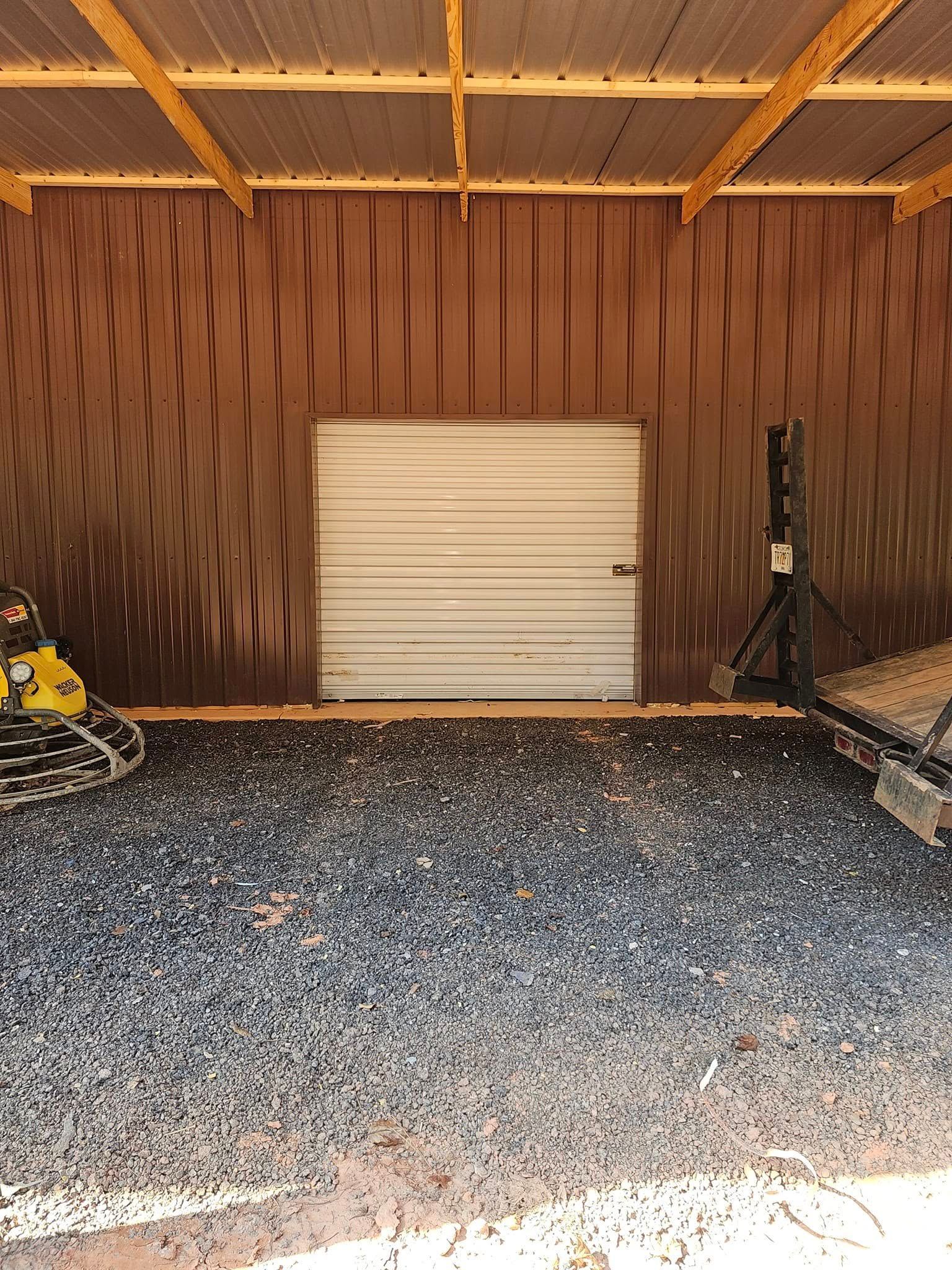 A shed interior with a gravel floor, metal door, and corrugated metal walls and ceiling.