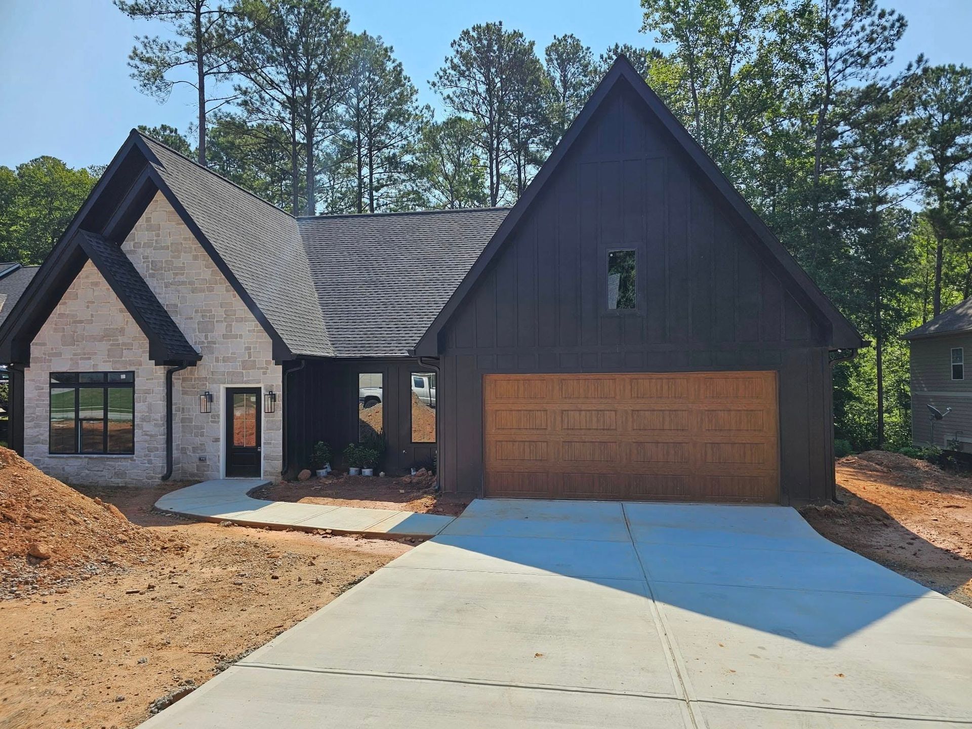 Modern home with stone and dark siding, tan garage door, concrete driveway.