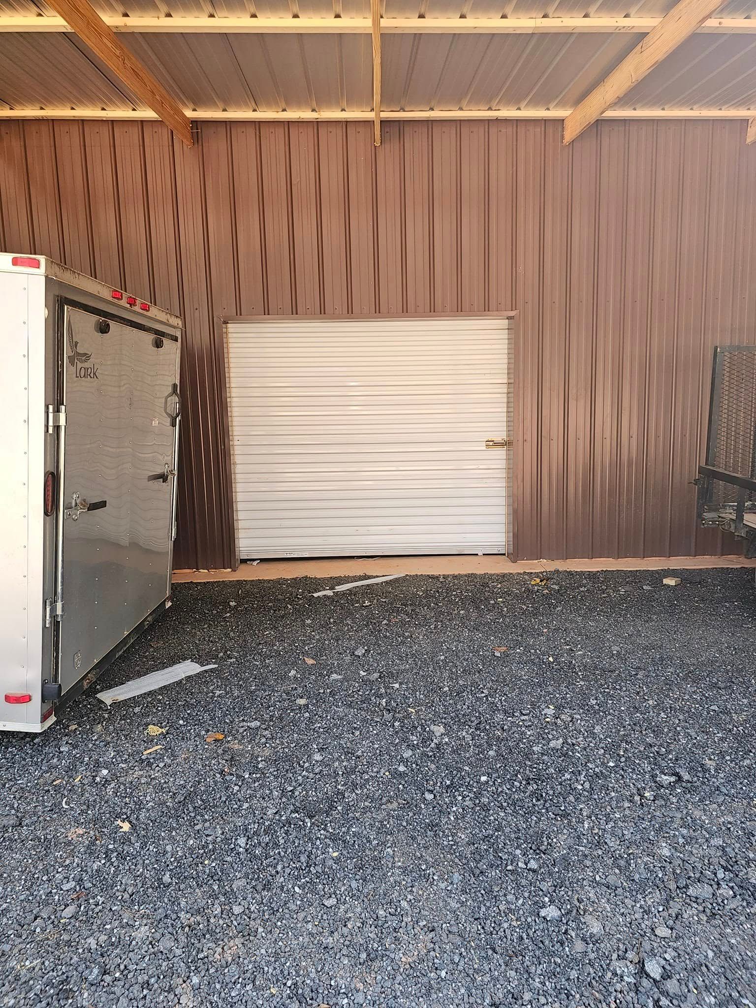 Open trailer next to a corrugated metal wall and a gravel floor.