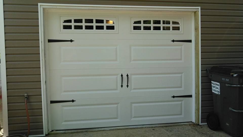 White garage door with decorative black hinges and handles, set against brown siding.
