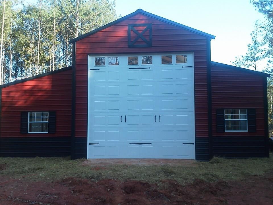 Red and black barn-style building with white garage door and small windows, set in a wooded area.