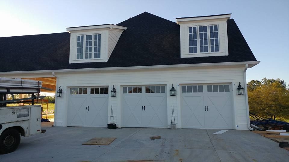 White three-car garage with black roof, two dormer windows, and exterior light fixtures.