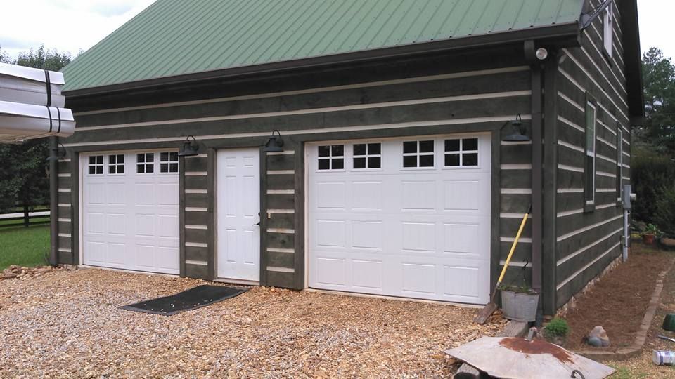 Log cabin-style two-car garage with white doors, green roof, and gravel driveway.