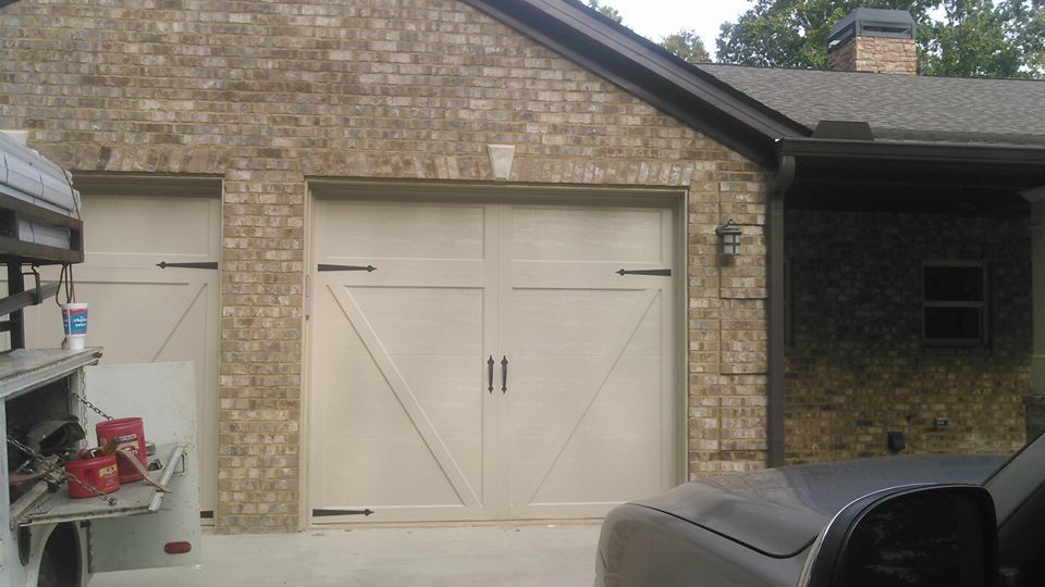 Tan garage doors with black handles, set in a brick building. A side service truck and car are visible.