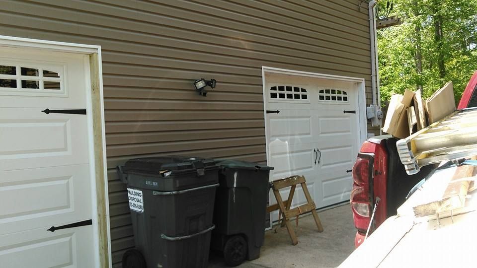 Garage exterior with brown siding, white doors, trash bins, and a red truck with debris.