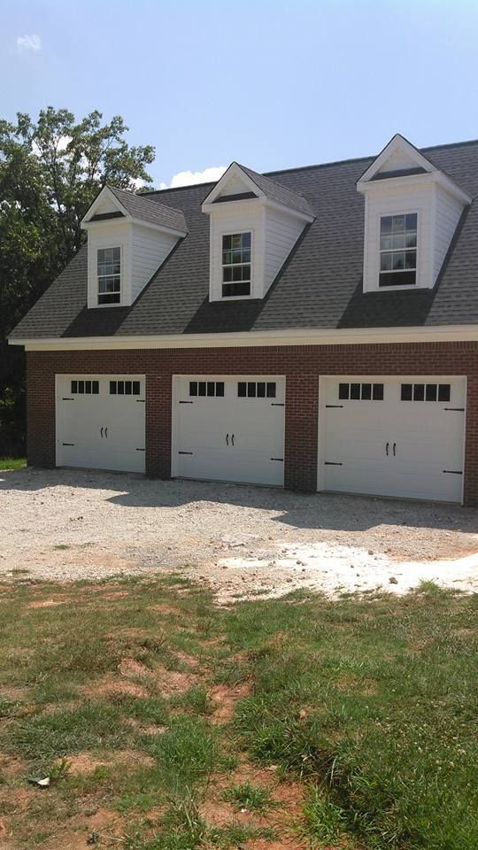 Brick garage with three white doors, three dormer windows on the roof, gravel driveway.