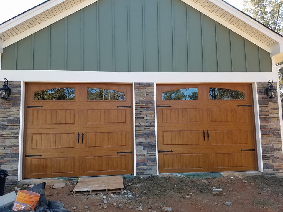 Two brown garage doors with arched windows, stone accents, and green siding.