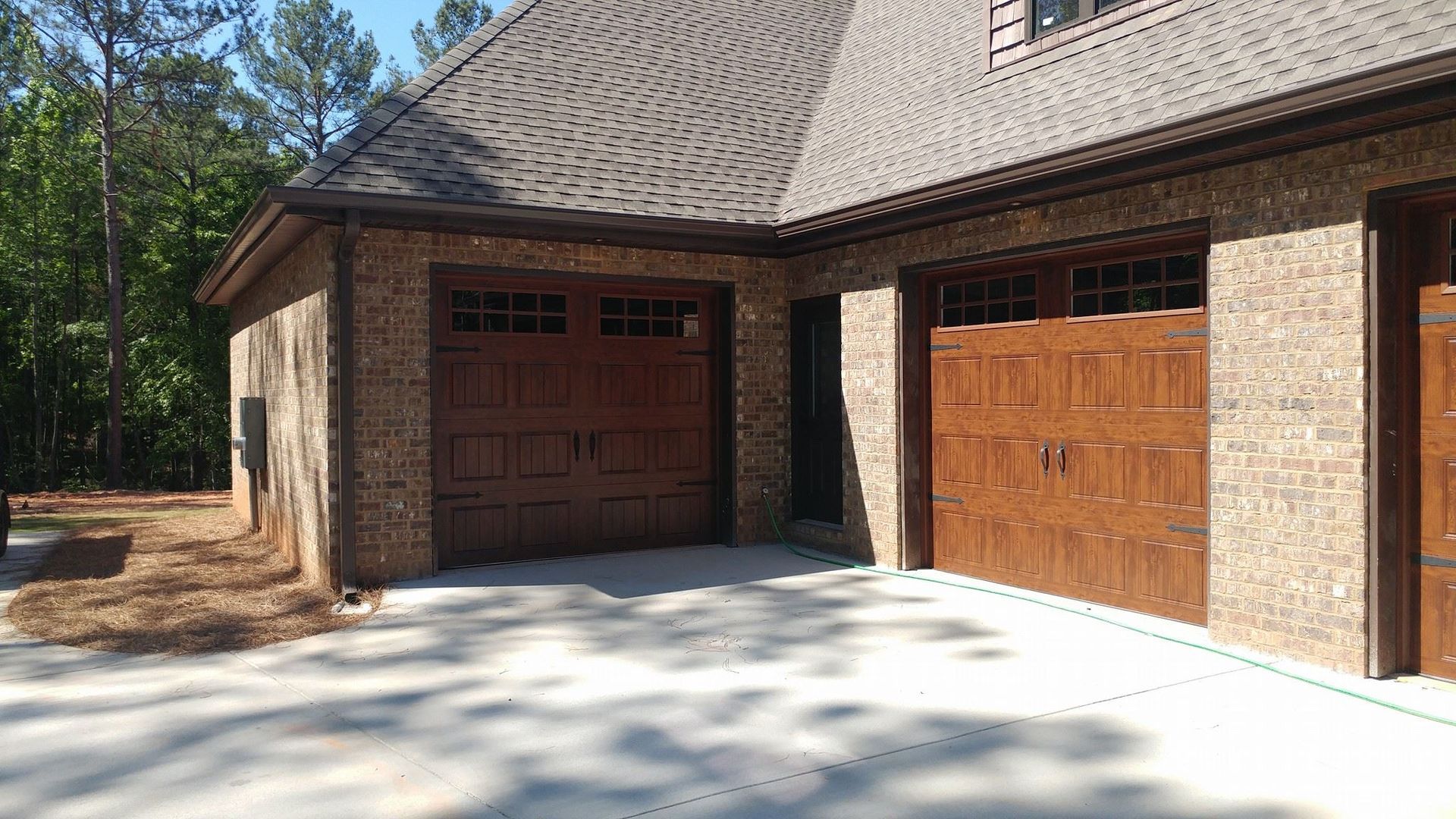 Brown brick garage with three wooden doors under a textured roof, set on a concrete driveway.