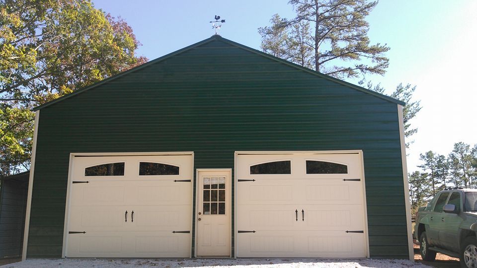 Green metal garage with two white garage doors and a small white door in the center.