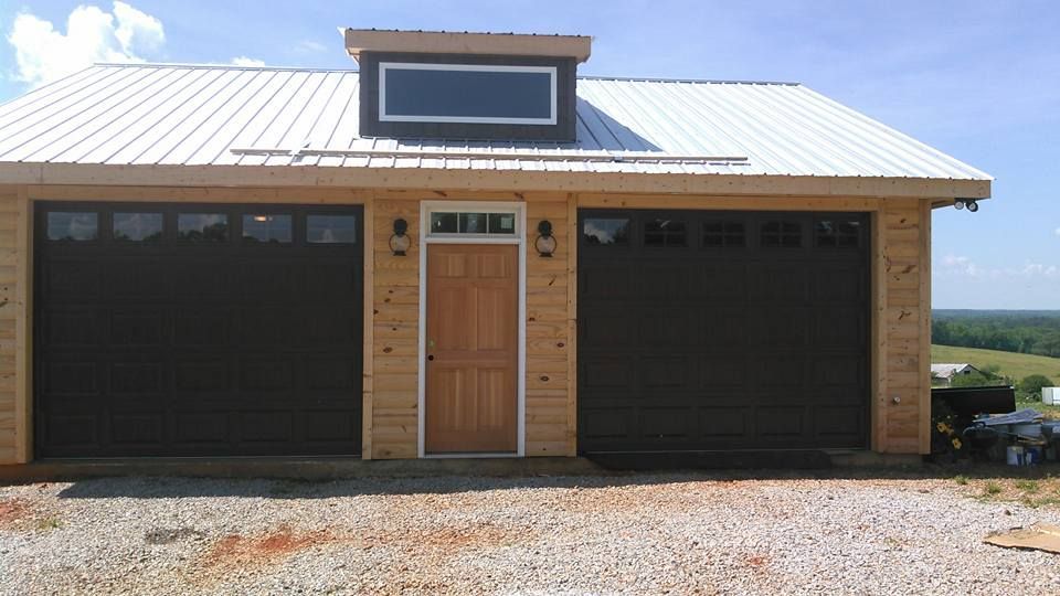 Garage with two dark garage doors, light wood siding, light wood door, and a white metal roof.