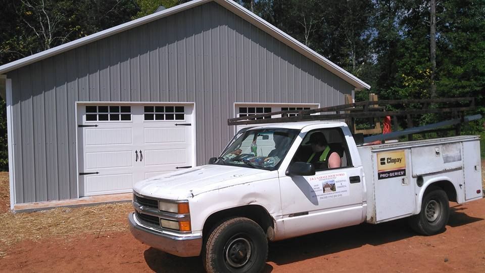 White truck parked in front of a gray garage. Truck has a work bed and a person is visible.