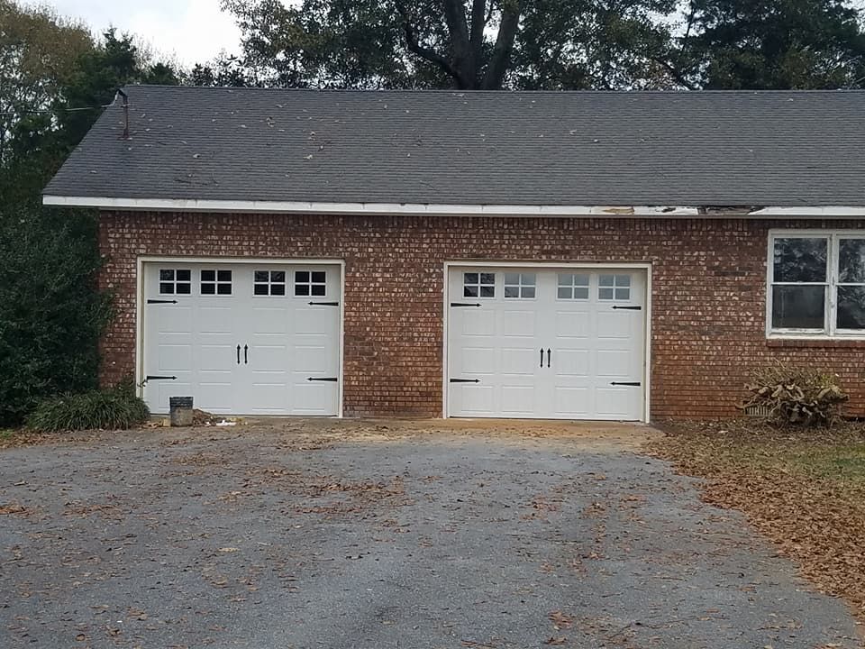 Two white garage doors on a brick building with a gravel driveway.