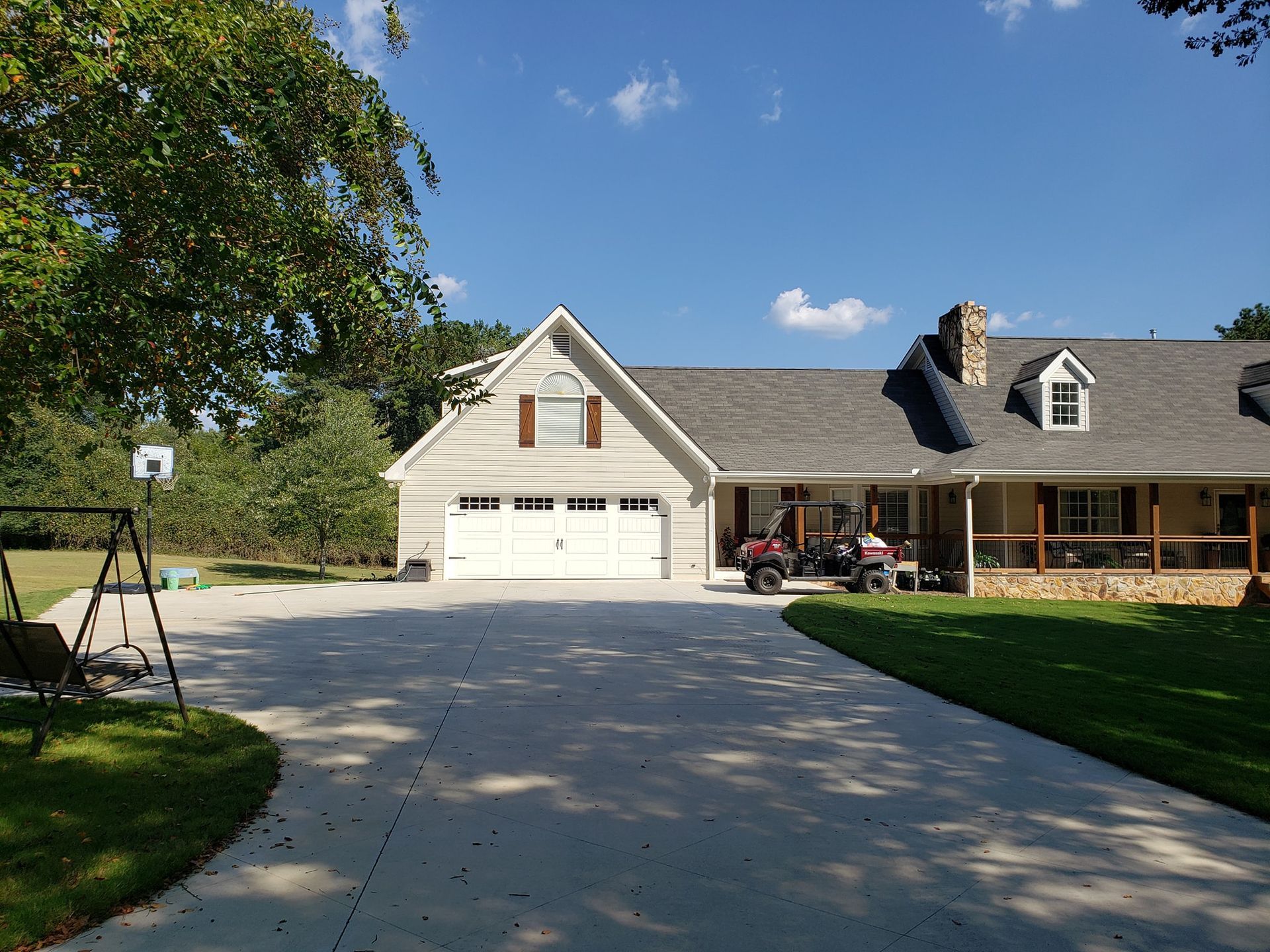 House with driveway, garage, and porch; blue sky and trees in background.