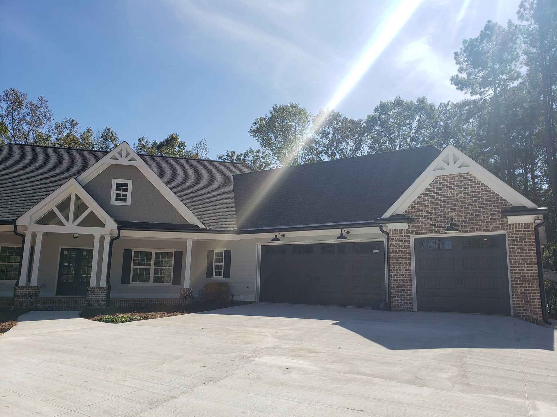 Two-story house with gray stucco, brown garage doors, and brick accents under a sunny sky.