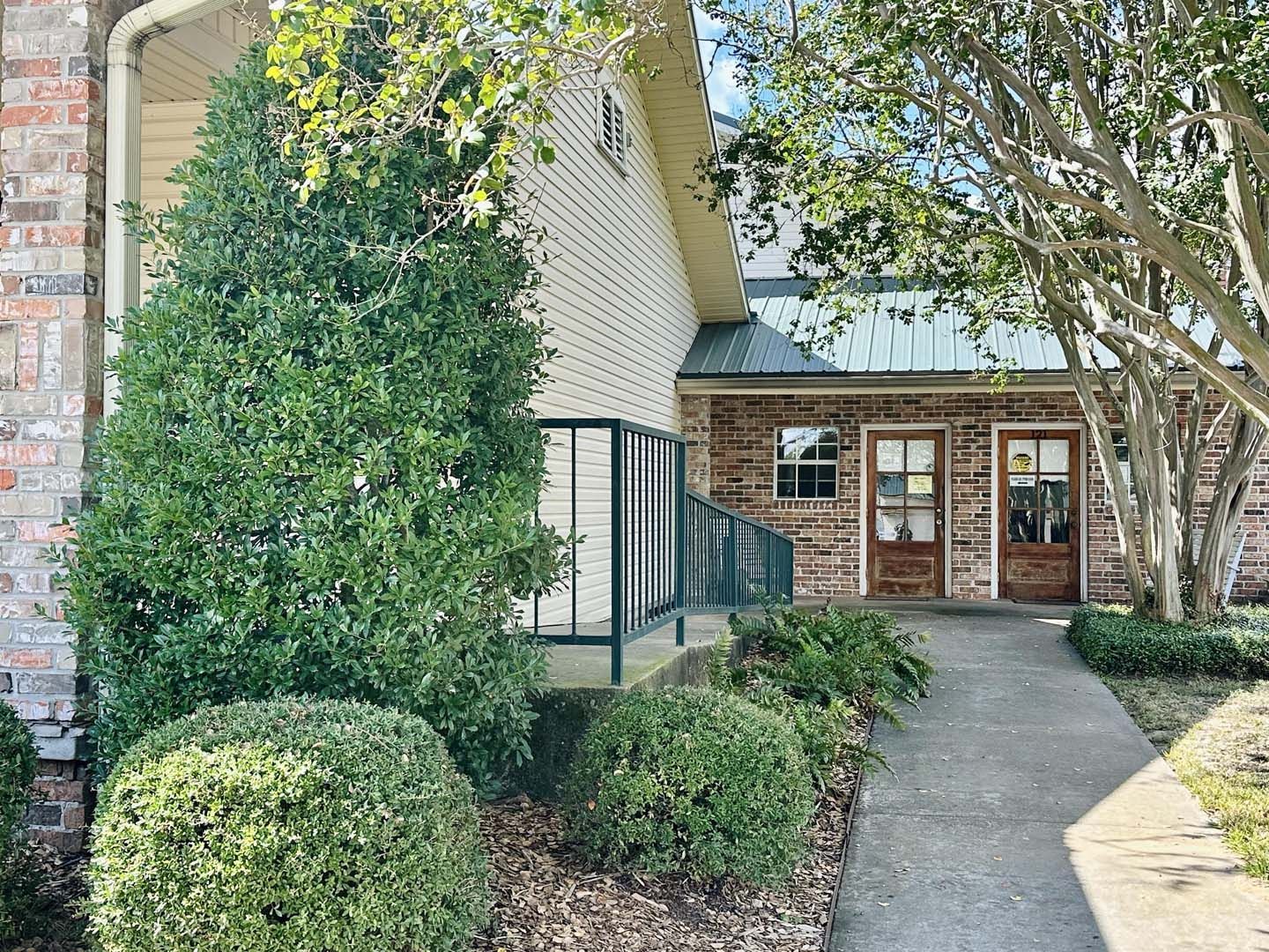 Exterior of a brick building with a walkway, green bushes, and two wooden doors.