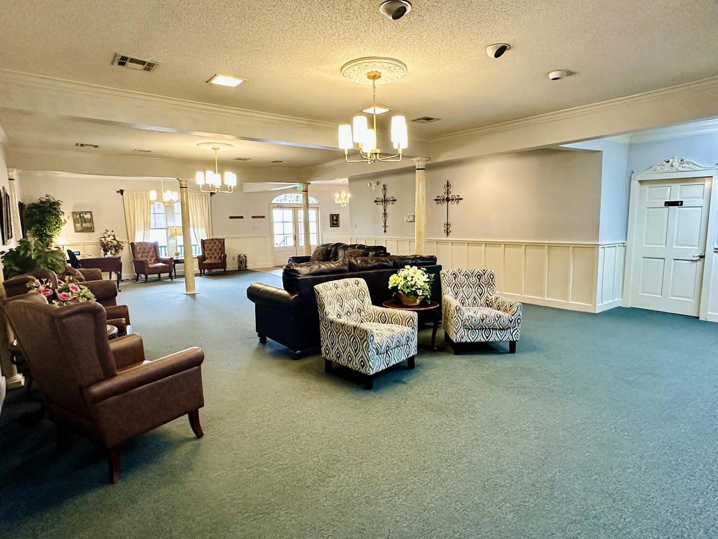 A large waiting room with chairs and couches, green carpet, and chandeliers.